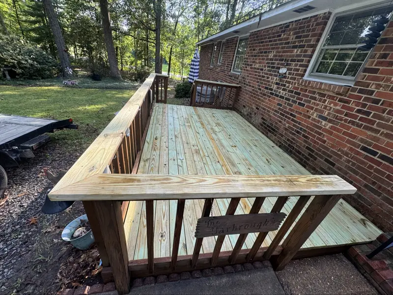 New wooden deck with railing beside a brick house